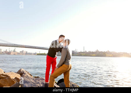 Mann küssen Freund beim Stehen auf Felsen von East River an einem sonnigen Tag Stockfoto