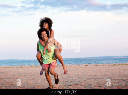 Mann huckepack Freundin am Strand gegen Sky Stockfoto