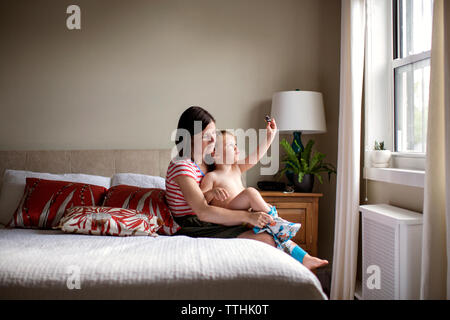 Mutter dressing verspielten Sohn beim Sitzen auf dem Bett Stockfoto