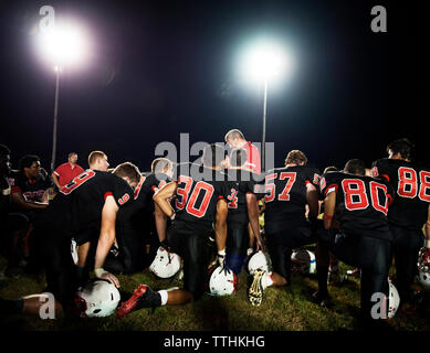 Ansicht der Rückseite des American Football Spieler kniend auf Leuchtfeld bei Nacht Stockfoto