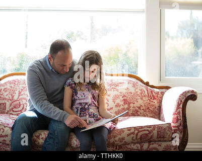 Vater lehre Tochter auf dem Sofa zu Hause Stockfoto