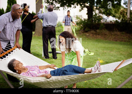 Happy girl Suchen an der älteren Frau liegen in der Hängematte mit Familie im Hintergrund bei Hinterhof Stockfoto