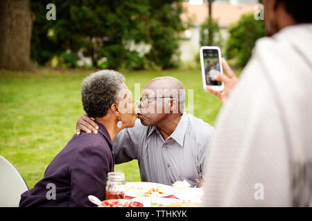 7/8 Bild der Frau fotografieren Senior paar Küssen im Hinterhof Stockfoto