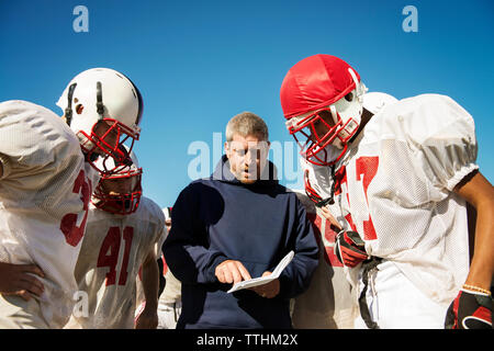 Trainer gemeinsame Strategie zu American Football Spieler stehen auf dem Feld Stockfoto