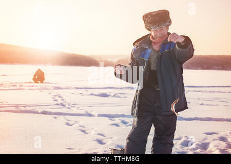 Portrait von älteren Mann mit Fisch beim Stehen auf gefrorenem See Stockfoto