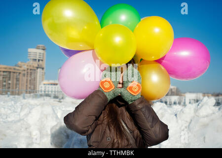 Frau mit bunten Ballons mit Gesicht mit den Händen in Park Stockfoto