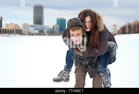 Portrait von glücklichen Mann huckepack mit Freundin auf Schnee im Park Stockfoto