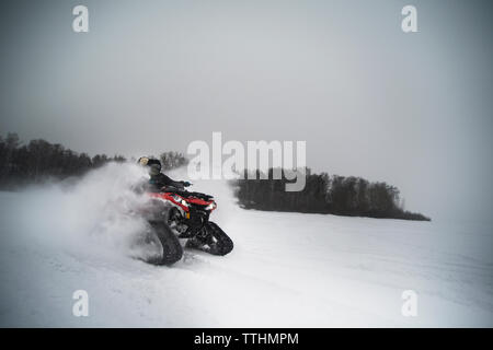 Freunde reiten Schneemobil auf Feld gegen Sky Stockfoto