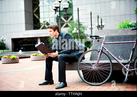 Geschäftsmann mit Mappe, während er am Fahrrad auf dem Sitz sitzt Stockfoto
