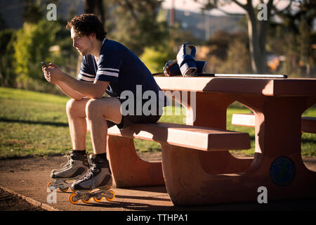 Roller hockey player mit Handy beim Sitzen auf der Werkbank Stockfoto