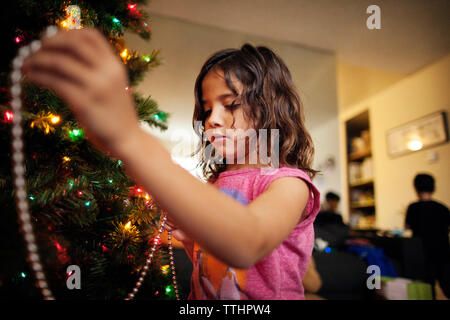 Mädchen, das zu Hause den weihnachtsbaum dekoriert Stockfoto