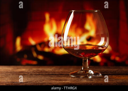 Ein Glas Cognac auf Holztisch mit Lagerfeuer Hintergrund Stockfoto