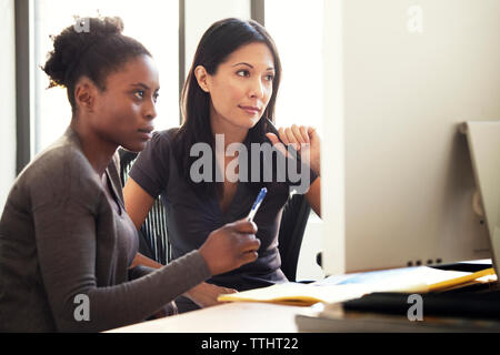 Geschäftsfrauen, die im Büro auf Stühlen sitzen, auf den Computer schauen Stockfoto