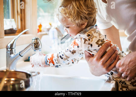 Zugeschnittenes Bild von Vater, Sohn und Waschen der Hände am Waschbecken Stockfoto