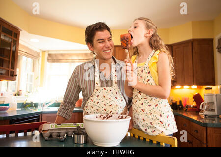 Tochter Löffel lecken, während der Vater in der Küche zu Hause stehend Stockfoto