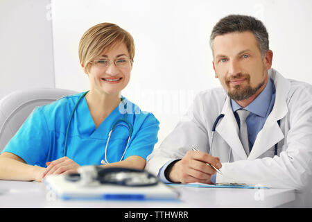 Männliche und weibliche Ärzte am Tisch sitzen im Krankenhaus, im Innenbereich Stockfoto