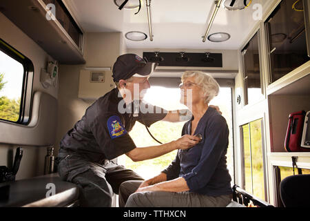 Sanitäter untersuchen Patienten mit Stethoskop während in Krankenwagen sitzen Stockfoto