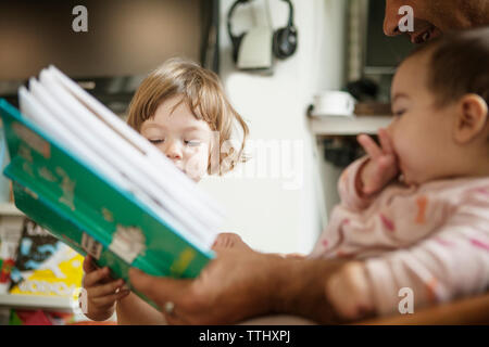 Zugeschnittenes Bild von Vater Holding buchen Sie beim Sitzen mit Töchter zu Hause Stockfoto