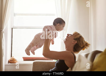 Glückliche Mutter anheben Baby Mädchen beim Sitzen auf dem Sofa zu Hause Stockfoto