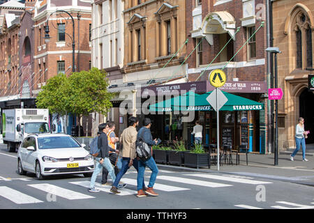 Männer, die über die Straße in the Rocks in Sydney neben Vermögen der Krieg Sydney älteste Pub und ein Starbucks Cafe, Sydney, Australien Stockfoto