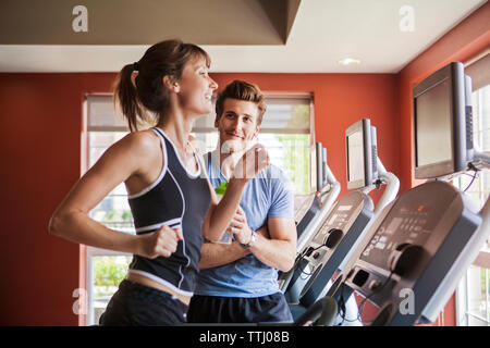Mann an Frau auf Laufband im Fitnessstudio suchen Stockfoto