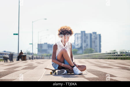 Teenager hören Musik beim Sitzen auf Skateboard Stockfoto