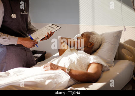 Älterer Mann an Arzt, während auf dem Bett im Krankenhaus liegend Stockfoto