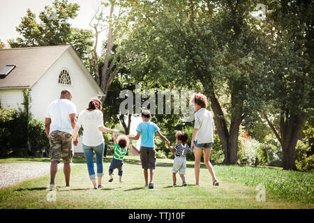 Ansicht der Rückseite des Familie Hand in Hand beim Gehen auf Wiese im Hinterhof Stockfoto