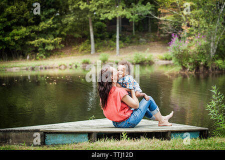 Mutter küssen Sohn sitzend auf Steg am See Stockfoto