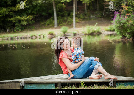 Glückliche Familie sitzen auf Steg am See Stockfoto