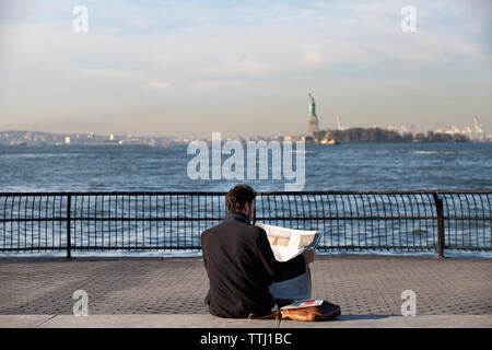 Mann News lesen Papier beim Sitzen auf der Promenade gegen Hudson River Stockfoto