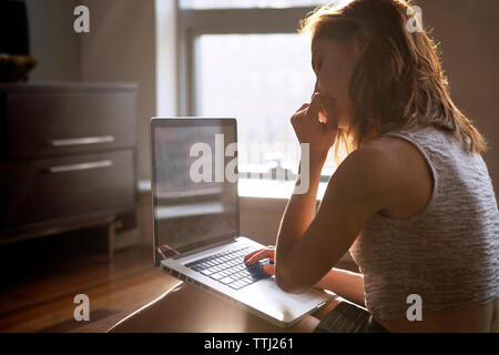 Nachdenkliche Frau mit Laptop, während zu Hause sitzen Stockfoto