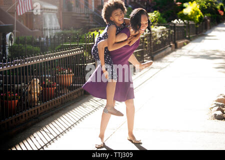 Tochter, piggyback Ride von ihrer Mutter Stockfoto