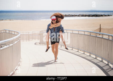 Glücklicher Mann huckepack Frau beim Spaziergang auf der Promenade am Strand Stockfoto