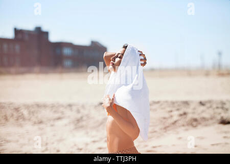 Frau mit Handtuch auf dem Kopf stehend am Strand gegen Sky Stockfoto