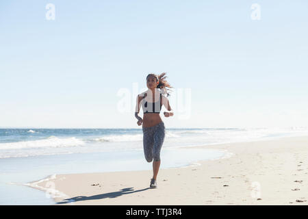 Selbstbewusste Frau joggen auf Ufer am Strand gegen Sky Stockfoto