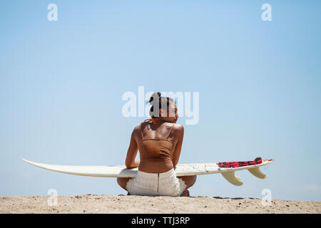 Rückansicht des Frau mit Surfbrett am Strand sitzen Stockfoto