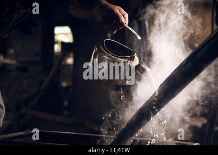 7/8 Hand der Schmied gießt Wasser auf Hot Rod in der Werkstatt Stockfoto