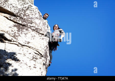 Low Angle View der Mann an der Freundin abseilen gegen den klaren blauen Himmel suchen Stockfoto