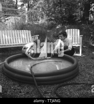 In den 1950er Jahren. Eine Mutter und Sohn an einem Sommertag. Der Junge spielt mit einem Modell Segelboot und setzt es im Wasser. Schweden 1954 Kristoffersson ref BP 35-2 Stockfoto