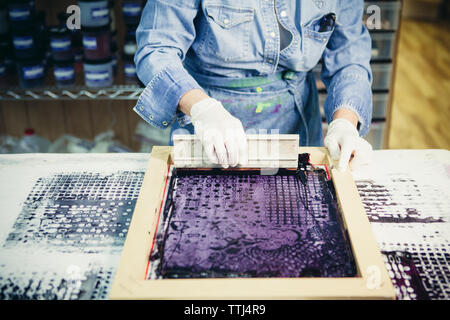 Mittelteil der handwerkerin mit Siebdruck Design auf Gewebe von Werkstatt zu drucken. Stockfoto