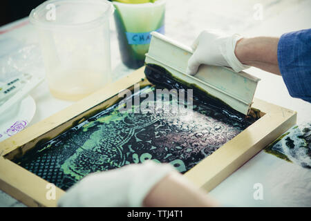 7/8 Hände der handwerkerin mit Rakel Design auf Gewebe von Werkstatt zu drucken. Stockfoto