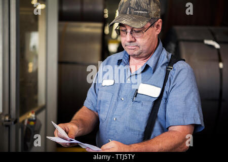 Ernste Arbeiter Prüfung der Dokumente beim Stehen in der Metallindustrie Stockfoto