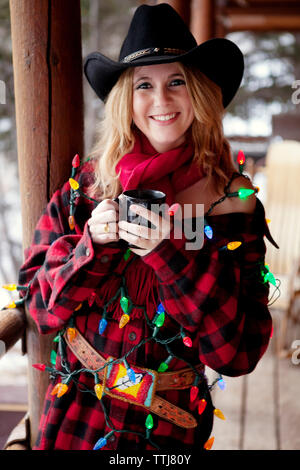 Porträt einer Frau mit weihnachtslichtern, die auf der Veranda steht Stockfoto