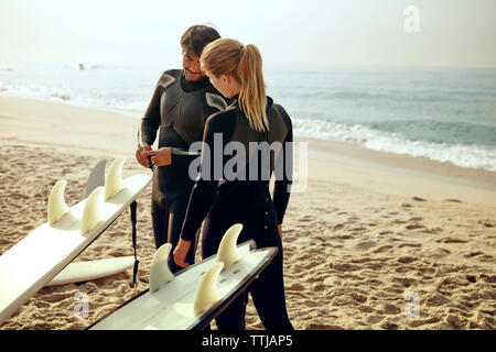 Mann auf Surfbrett stehend durch Frau am Strand Stockfoto