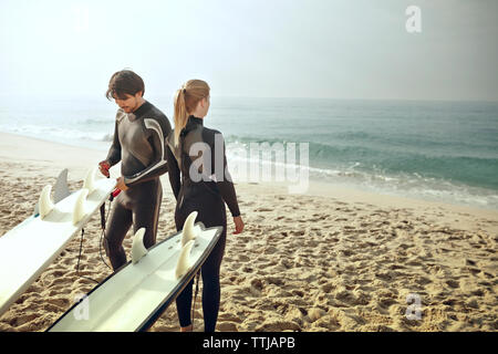 Der Mann und die Frau das Tragen von Neoprenanzügen von surfbrettern am Strand stehen Stockfoto