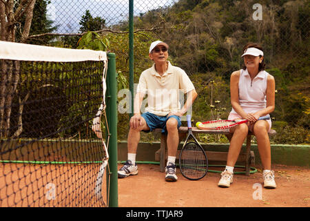 Senior Paar sitzt auf der Bank am Tennisplatz Stockfoto