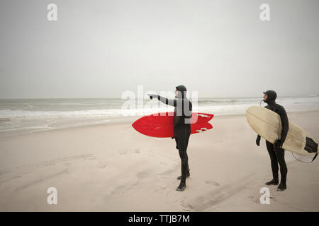 Freunde in Neoprenanzüge am Strand stehen Stockfoto