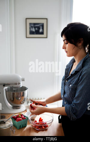 Frau schneiden Erdbeeren beim Stehen in der Küche zu Hause Stockfoto