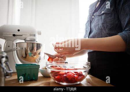 Mittelteil der Frau schneiden Erdbeeren, während durch die Arbeitsplatte in der Küche zu Hause stehend Stockfoto